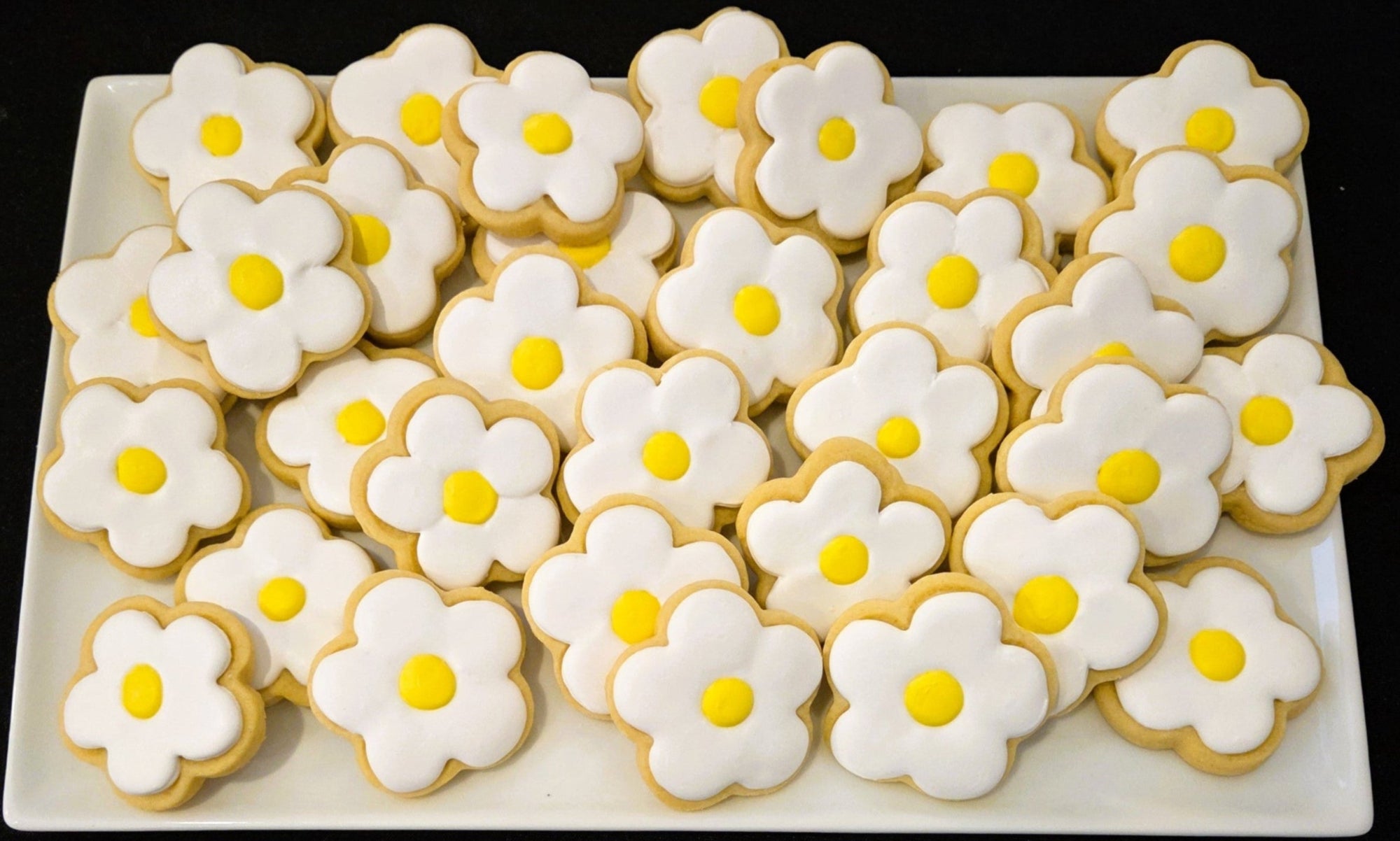 Decorative cookies shaped like daisies on a white plate with a black background